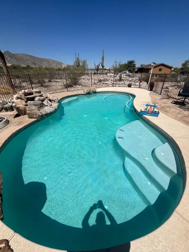 Kidney pool with a rock waterfall and a desert mountain beyond the iron fence