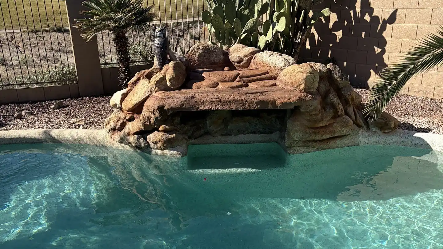 Rock grotto waterfall spilling into clear turquoise water, prickly pear on the wall